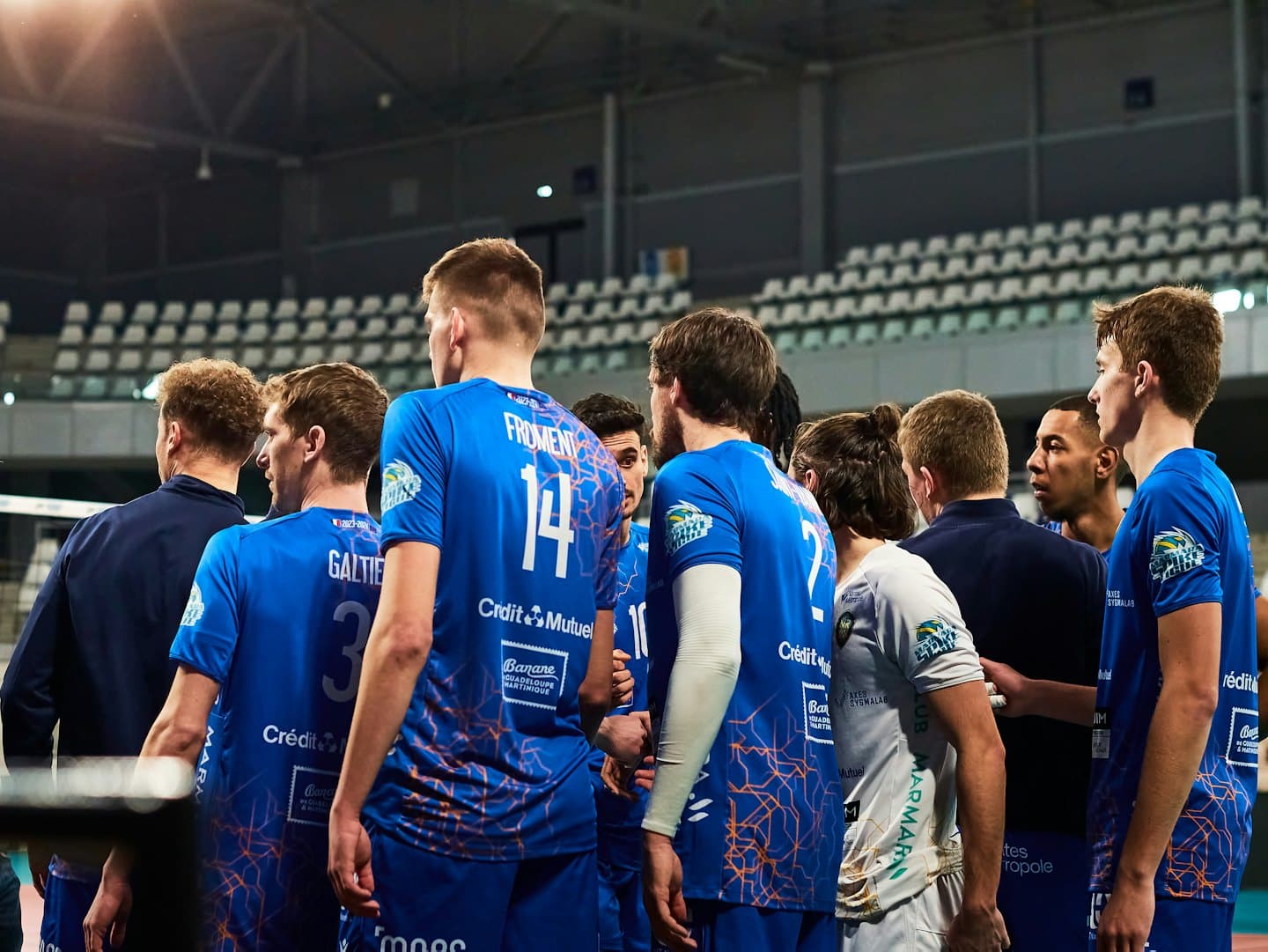Squadra di pallavolo riunita in cerchio ad ascoltare gli allenatori in campo.